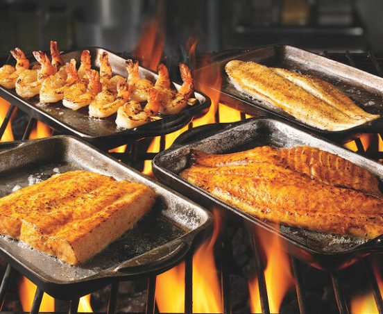 Trays of different seafood on top of a bbq grill